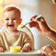 A happy baby sitting in a high chair, eagerly taking their first spoonful of mashed banana while being fed by a smiling parent. Perfect moment for introducing solid foods to babies.
